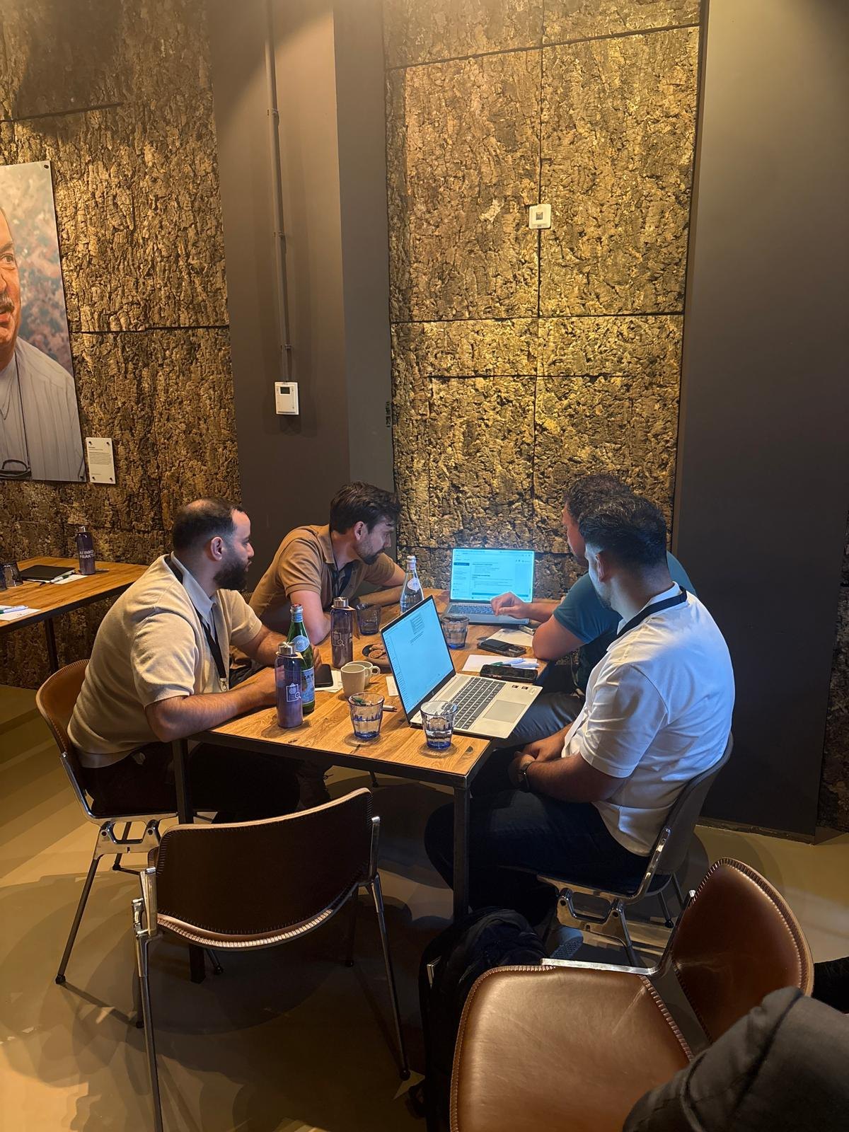 Vier deelnemers werken samen aan een tafel met laptops tijdens het eerste community-event.